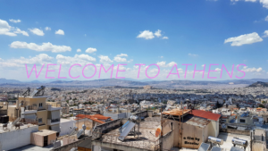 Skyline shot of Athens under a bright blue sky. Text reads Welcome to Athens.