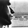 Still image from LA Plays Itself. Black and white image of a clean shaved man's profile, with a Movie Arcade sign in the background.