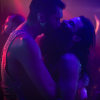 Still image from The Multiverse in a MouthFuck, showing two men in a tight embrace in a nightclub, bathed in purple light. 