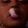 Still image from the short film, Snack Time, close-up of a black face with red lipstick, exhaling white smoke.