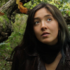 Still image from short film, Forest Affair. A dark haired feminine person looks towards the camera with a tree behind her. 